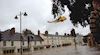 Helicopter flies above a flooded street as a man looks on