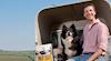 Farmer and sheep dog sit on edge of land rover