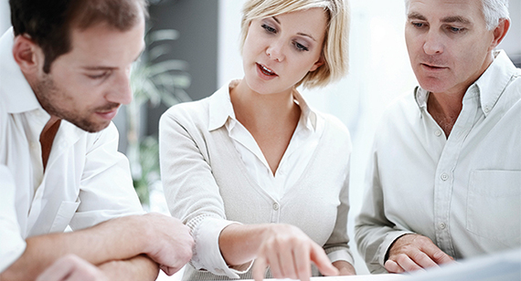 A lady is flanked by two men as they study business plans