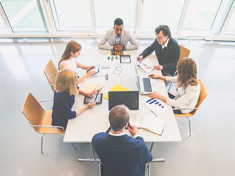 A business meeting in a light room involving three men and three women