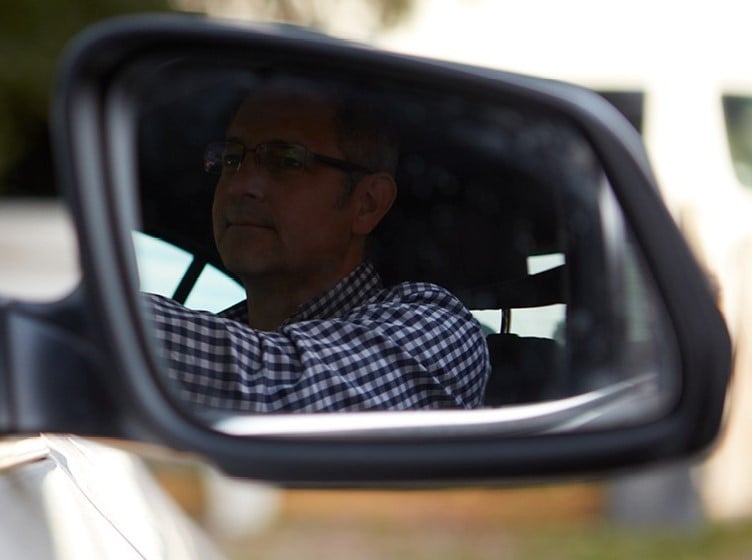 Male driver wearing gingham shirt in wing mirror of car