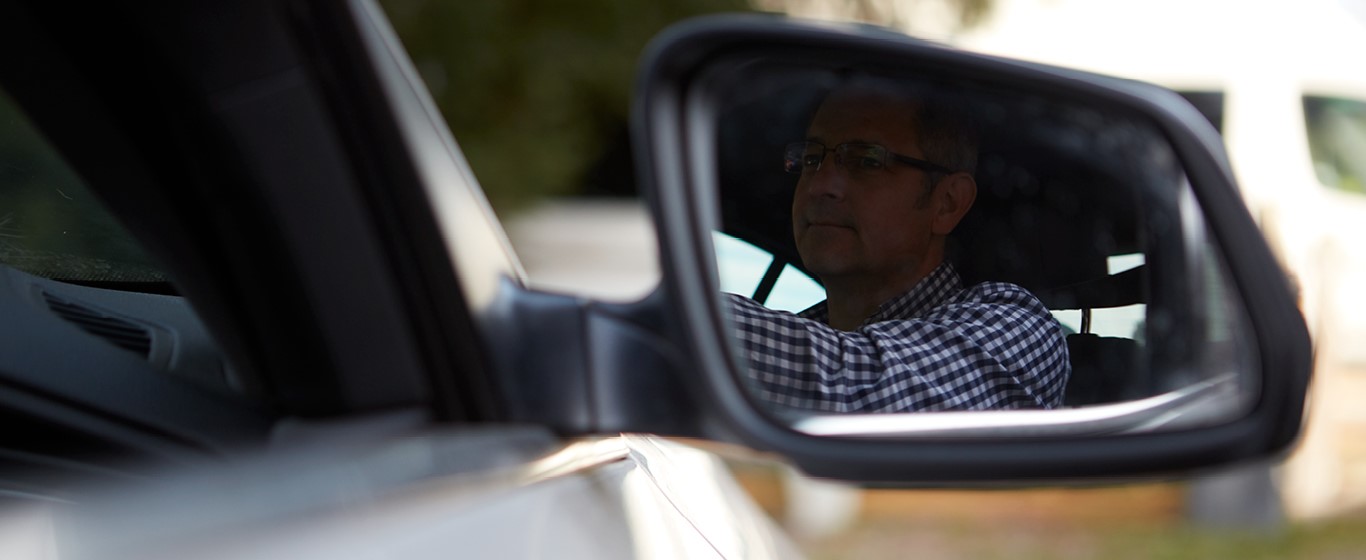 Male driver wearing gingham shirt in wing mirror of car