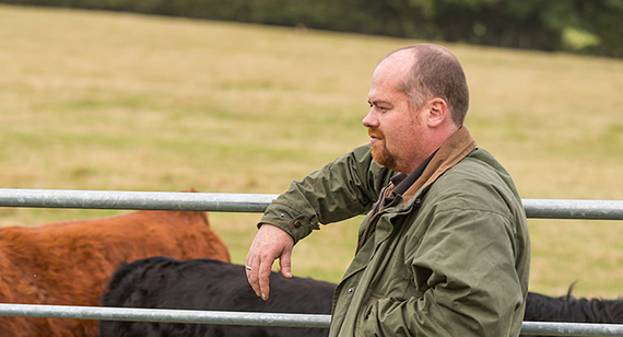 Cattle farmer wearing wax jacket leant against gate