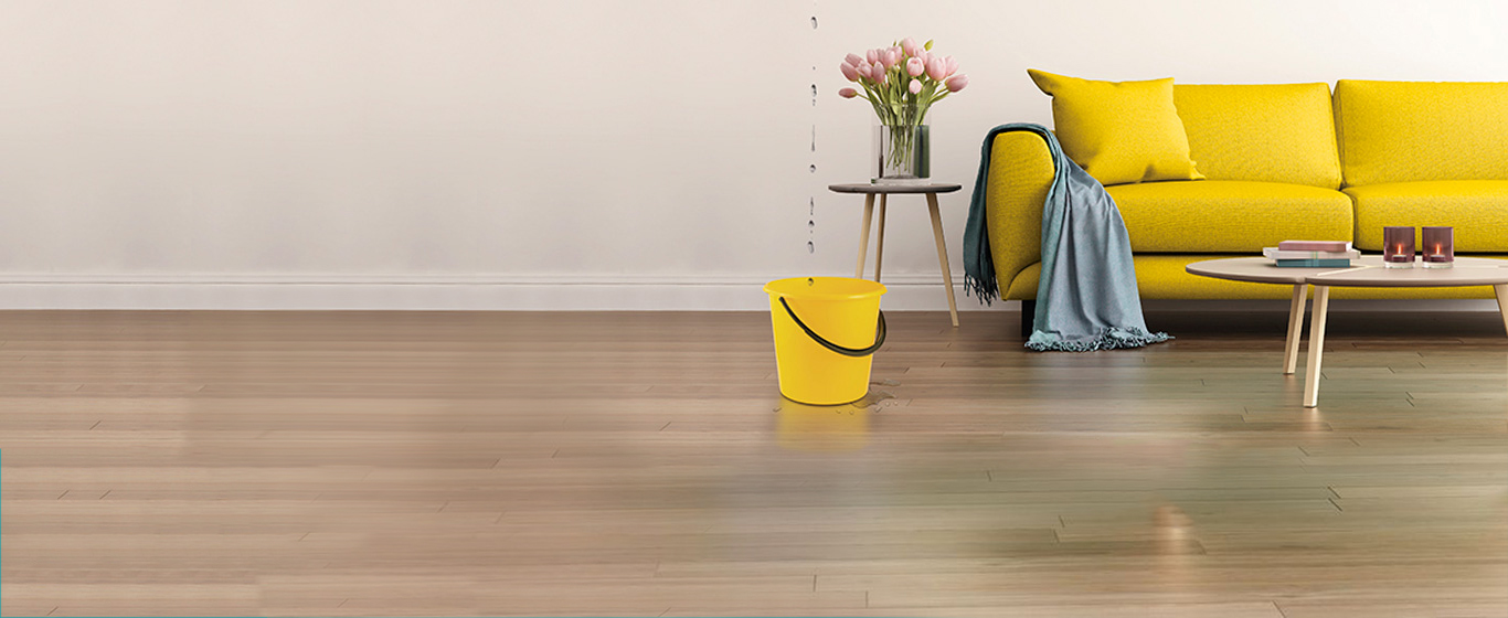Yellow sofa with throw draped over arm, yellow bucket catching water leaking from ceiling
