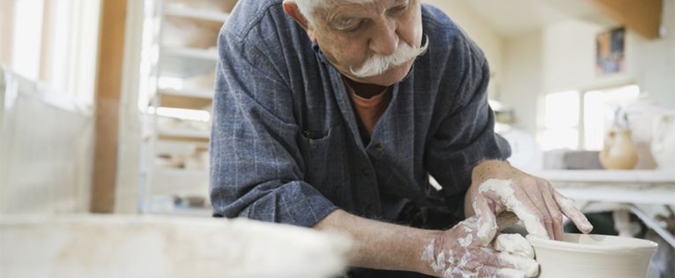 Grey haired man with moustache throwing and shaping clay pot