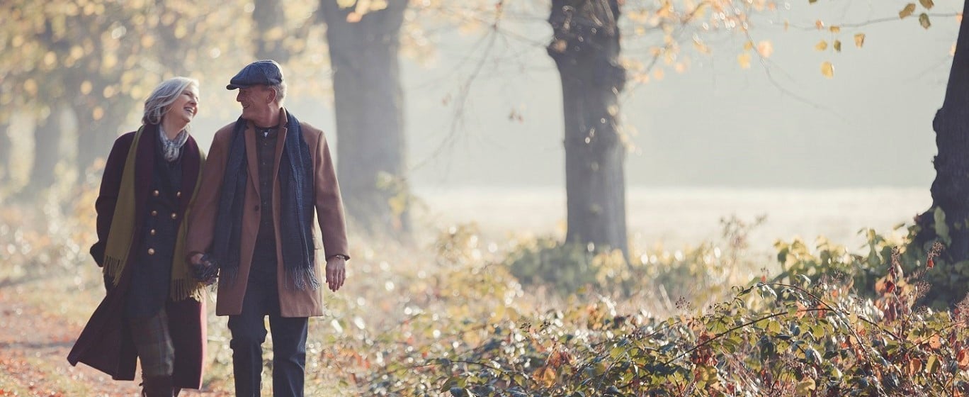 A middle-aged couple walking through woods on autumn day