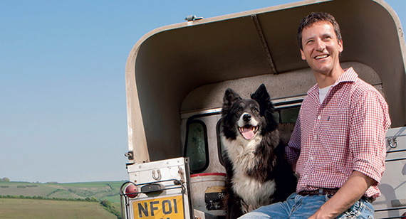 Farmer and sheep dog sit on edge of land rover