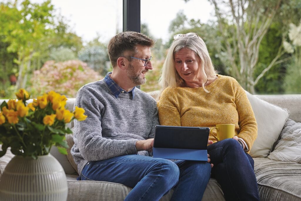 Man and lady in yellow jumper looking at an iPad on a sofa.